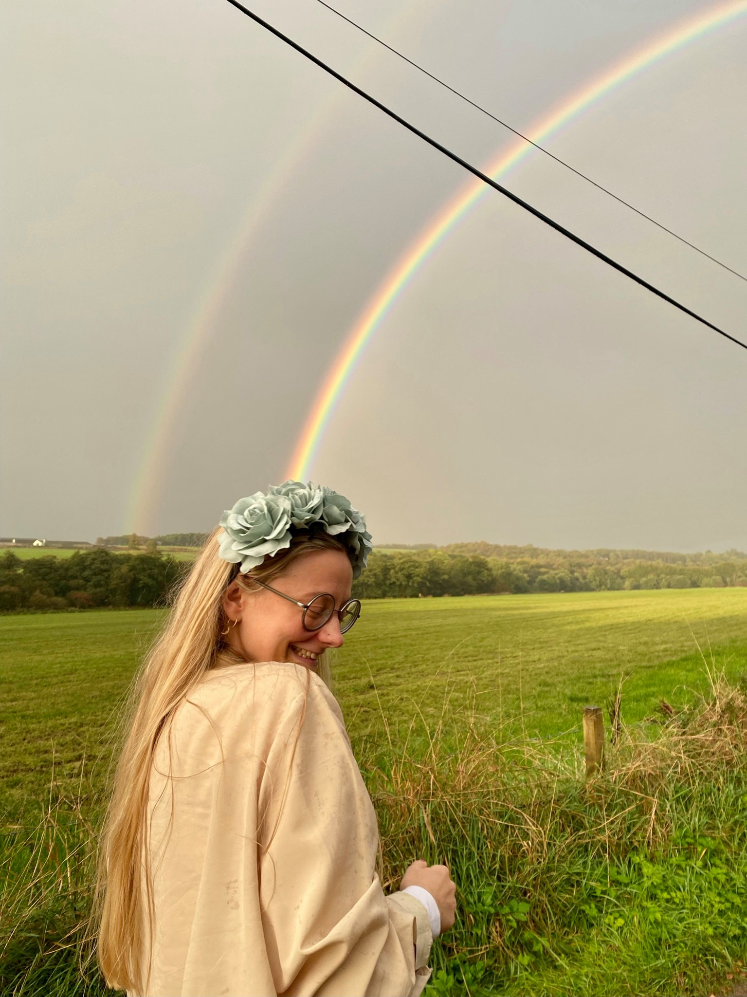 Cat smiles in front of a rainbow, wearing a flower headband and a yellow overshirt